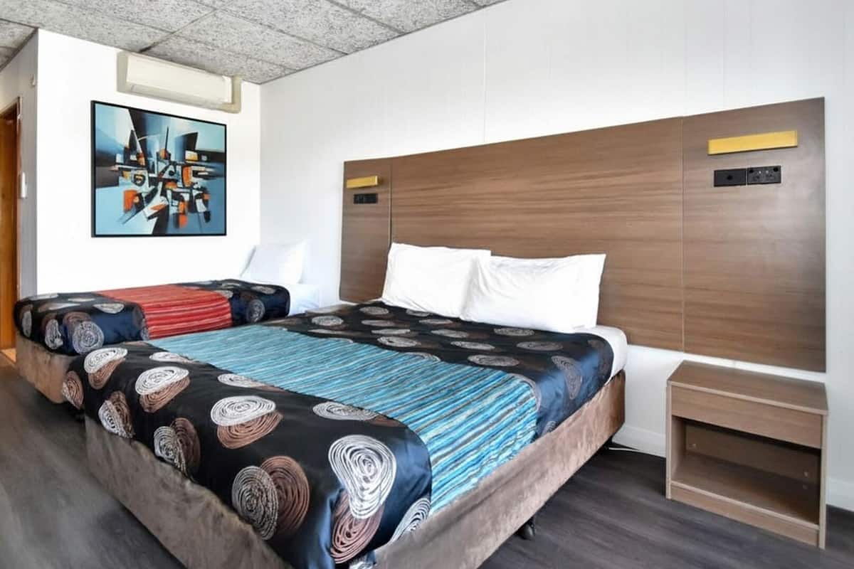 A hotel room with a large bed, a wooden headboard, a painting on the wall, and a wooden door.
