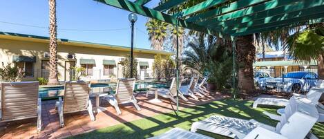 A poolside area with sun loungers, a palm tree, and a building in the background.