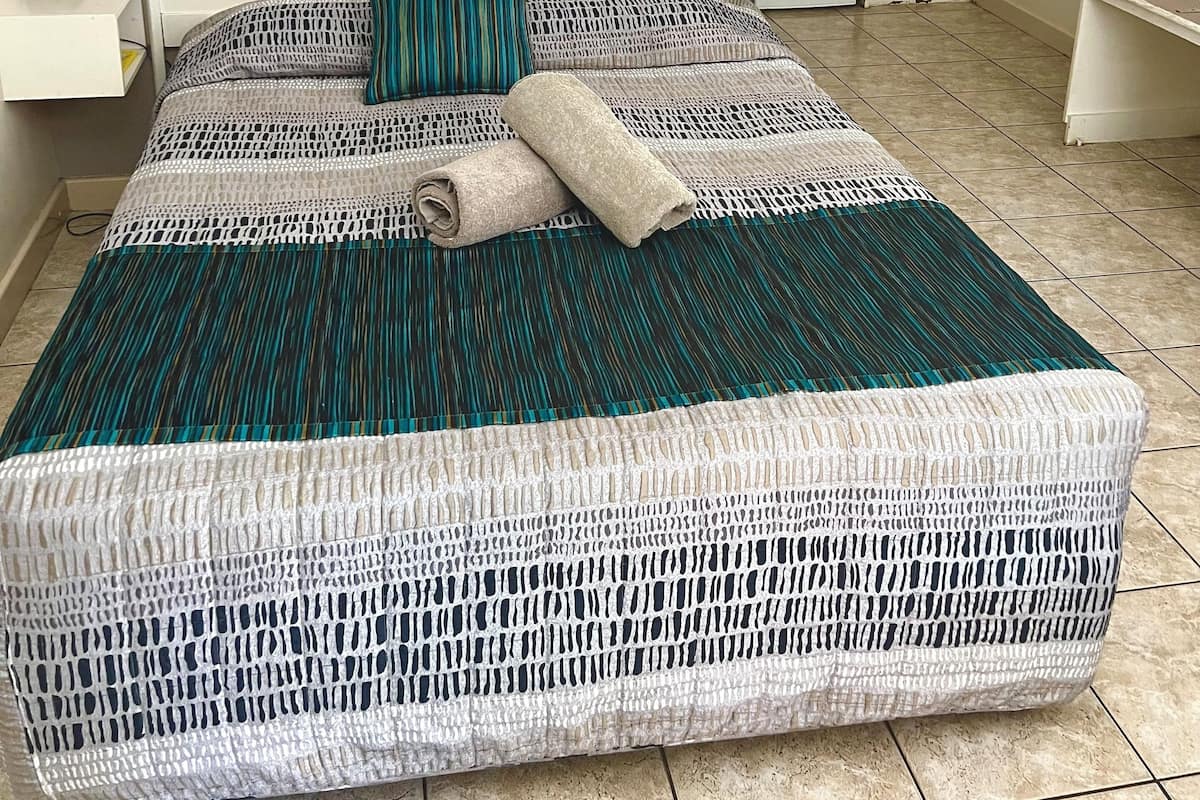 A neatly made bed with a patterned bedspread, a single pillow, and a rolled towel.