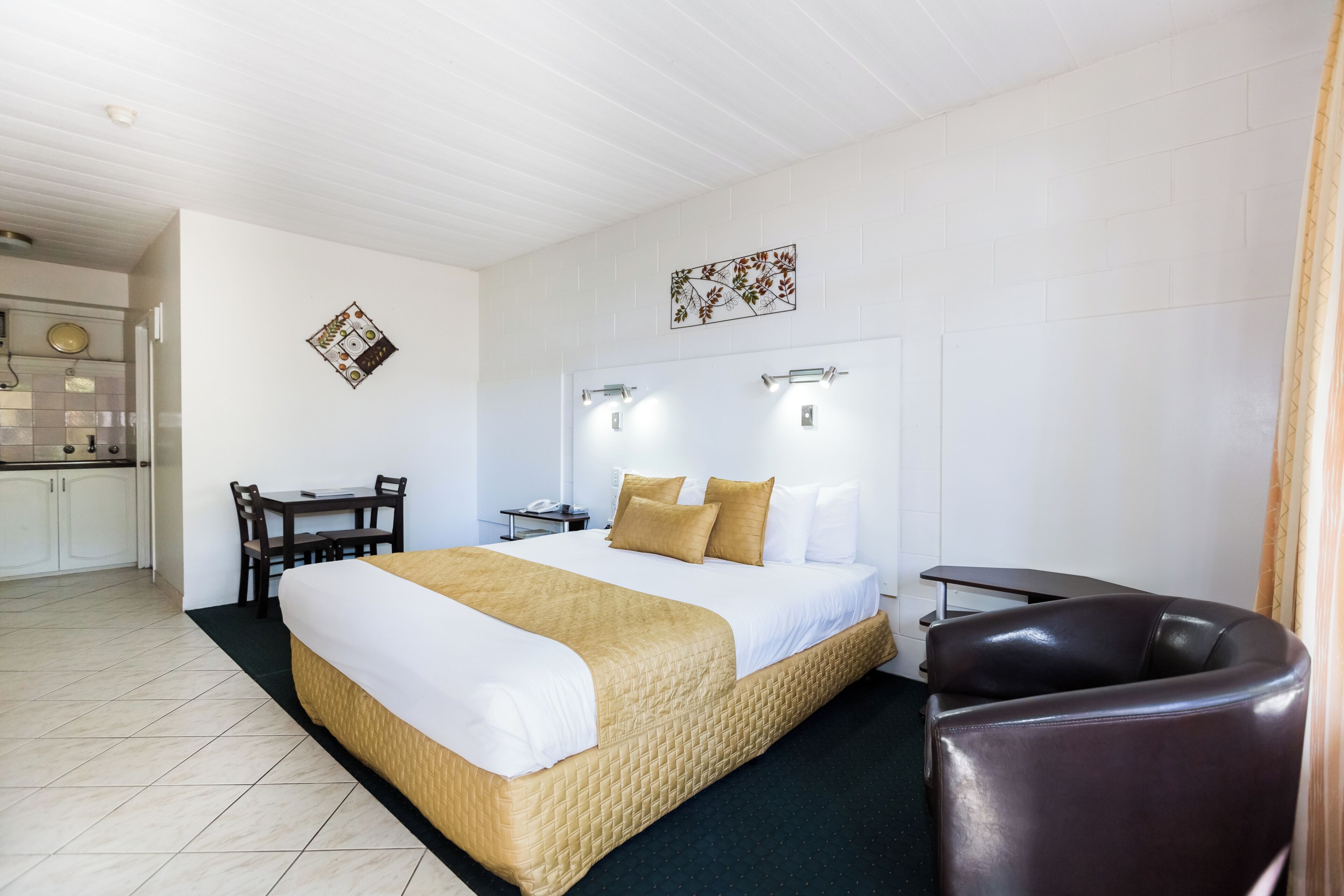 A hotel room with a bed, a desk, a chair, and a small kitchenette.
