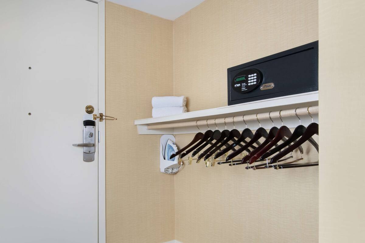 Ein Hotelzimmer mit weißer Tür, einem Schuhregal mit Schuhen, einem Handtuch und einer Bedienfeld.
