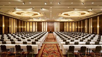 Un salón de conferencias amplio con filas de mesas y sillas, un pasillo central y una alfombra decorativa.
