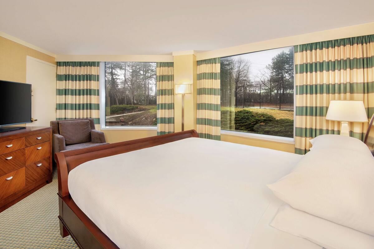 Ein Hotelzimmer mit einem großen Bett, einem Holzschrank, einem Fernseher und Blick ins Freie.