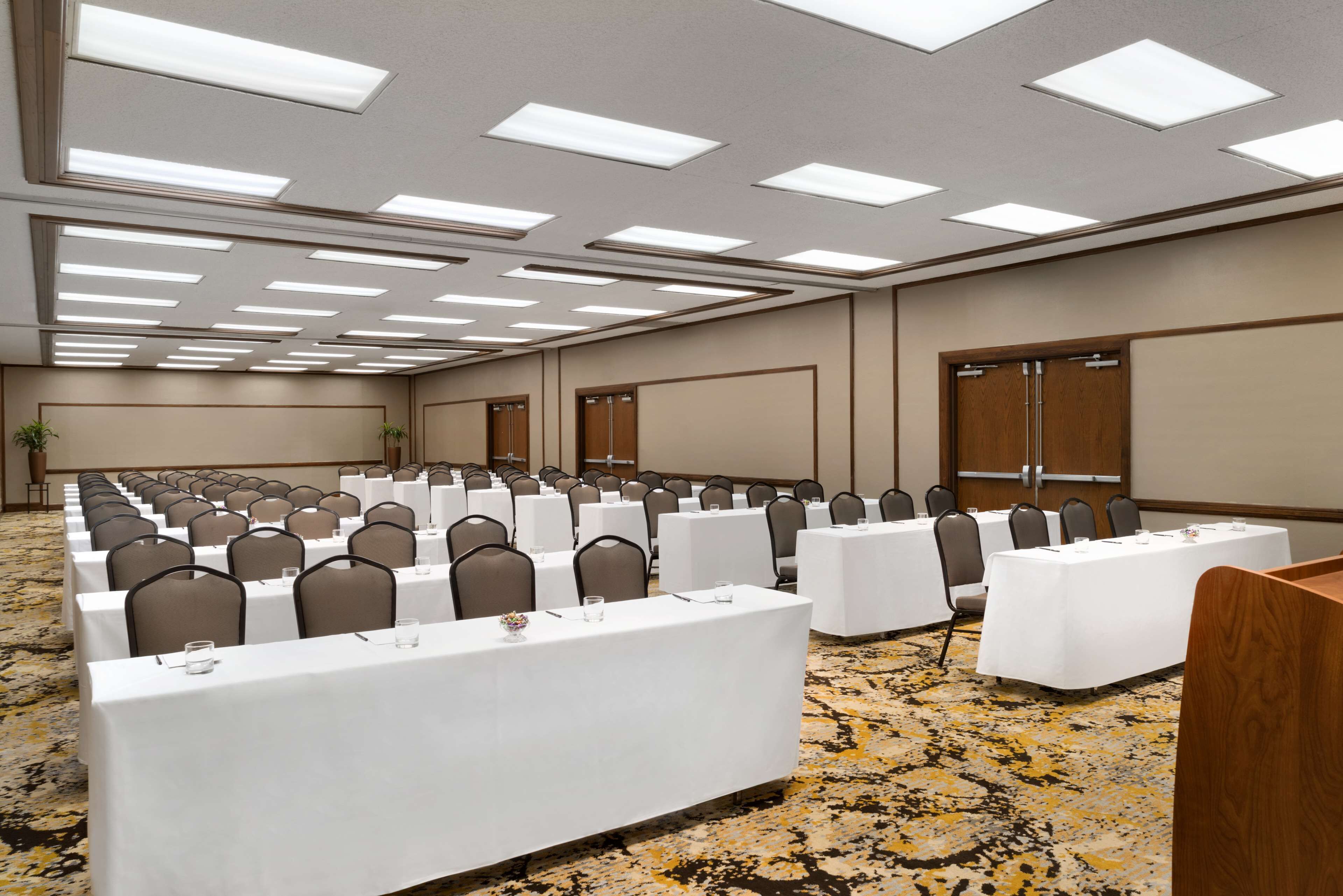 Un salón de conferencias con varias mesas y sillas, equipado con luces en el techo y piso alfombrado.