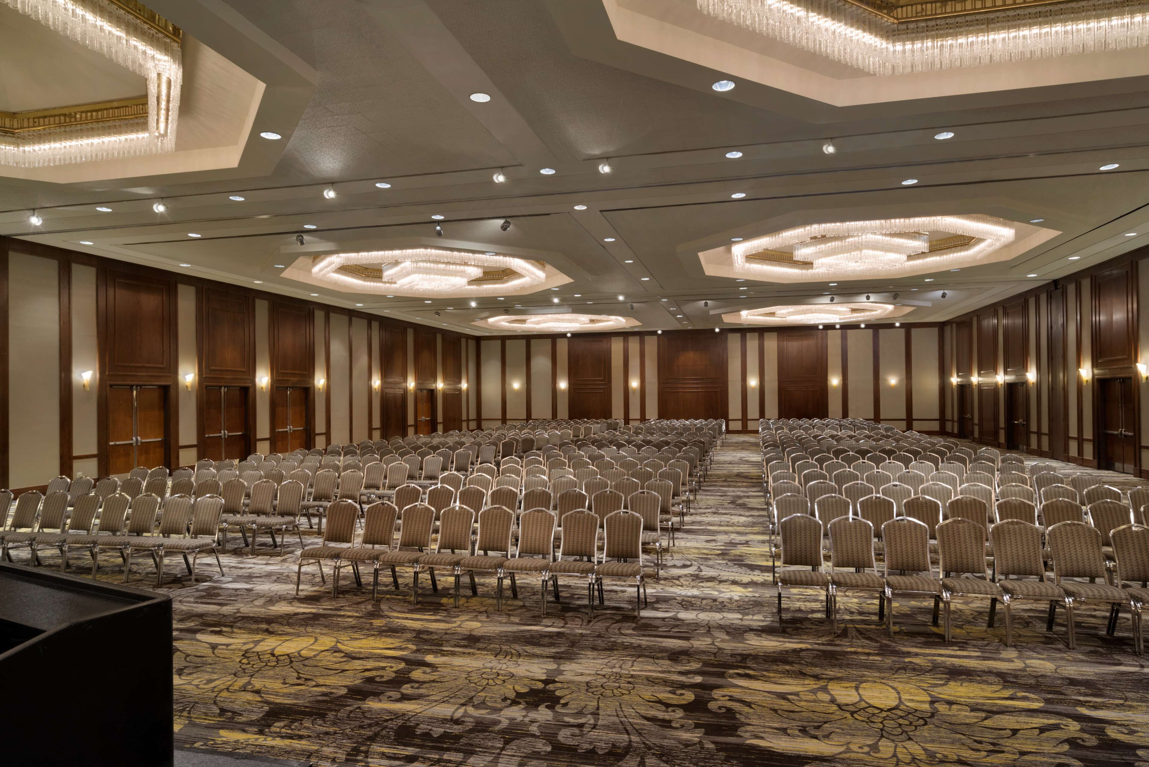 A large conference room with rows of chairs, a patterned carpet, and ornate ceiling lights.