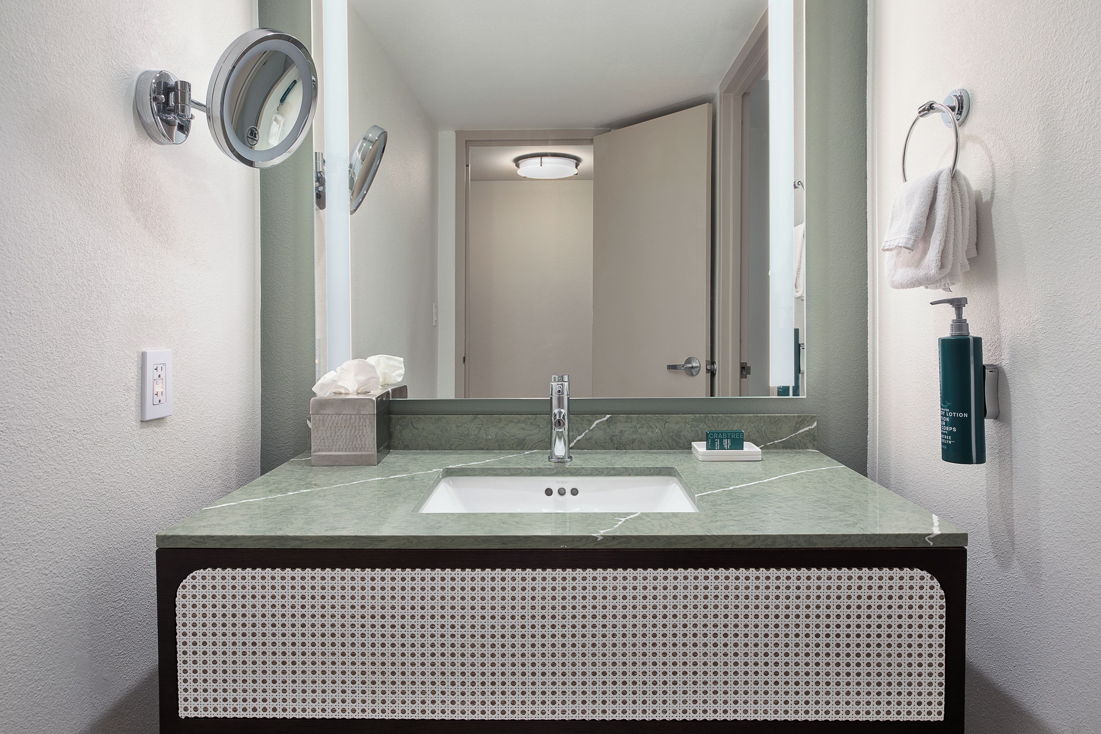 A bathroom with a sink, mirror, towel rack, and a bottle of lotion.