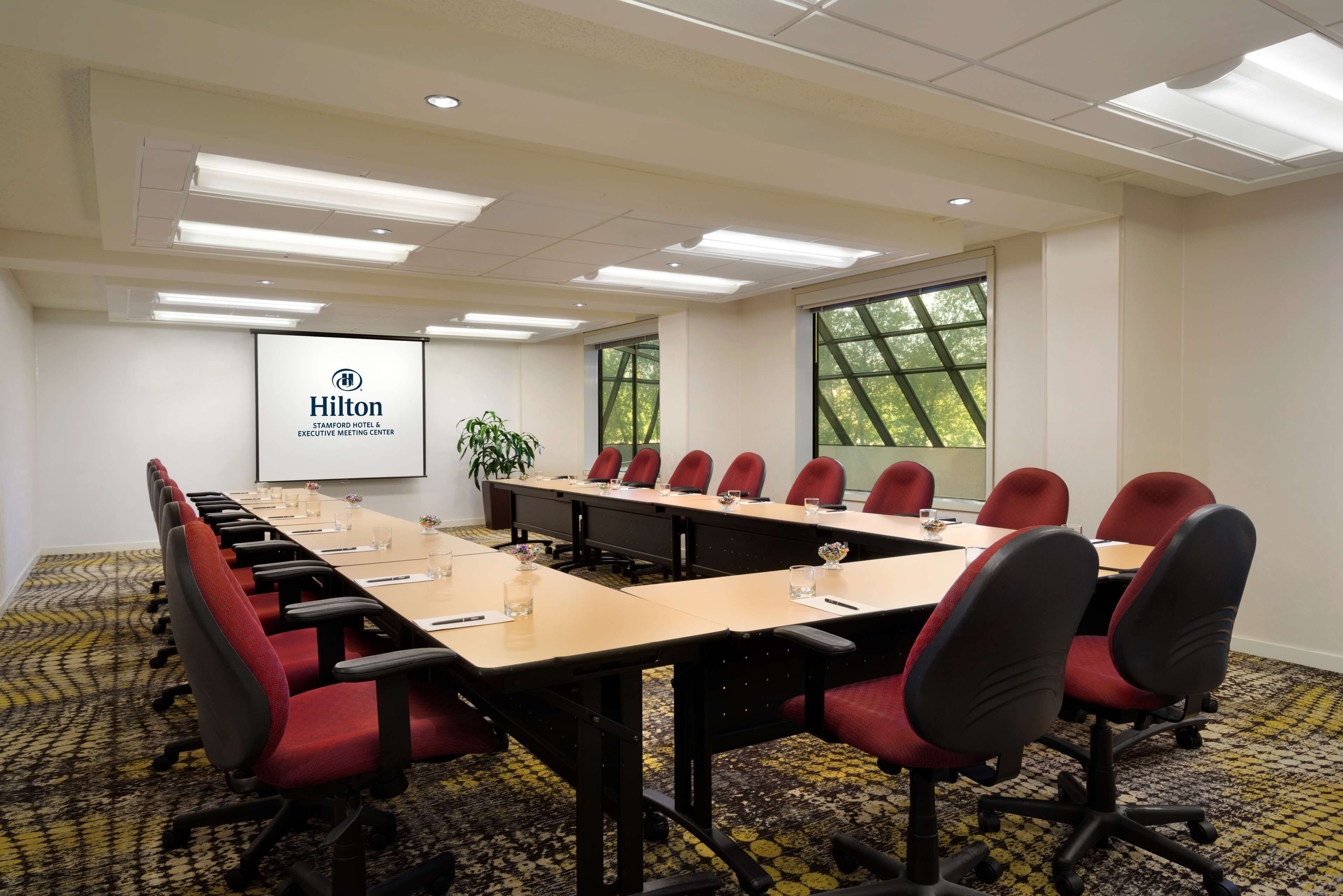 A conference room with a long table, red chairs, and a projector screen displaying the Hilton logo.