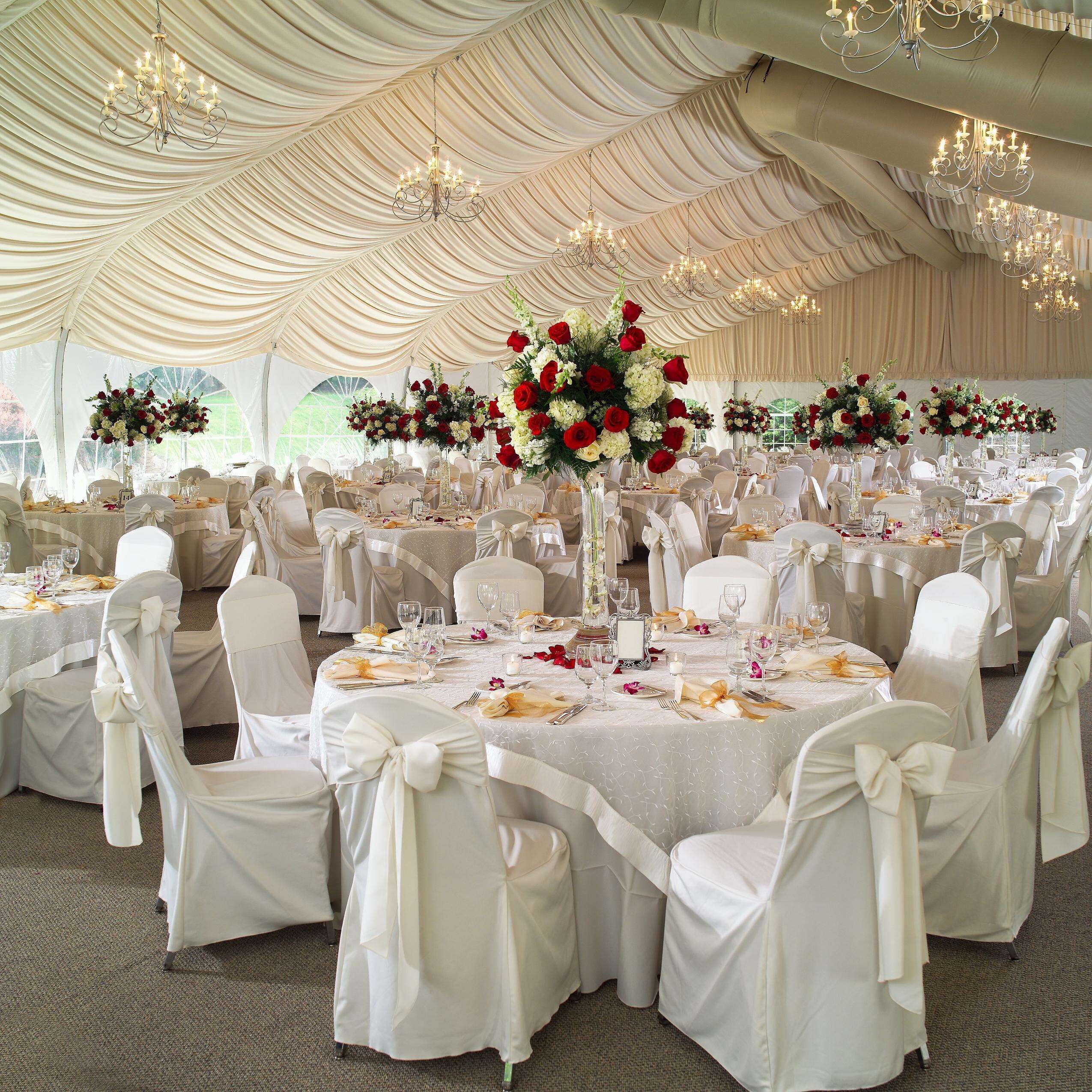 A banquet hall with round tables, white chairs, and chandeliers.