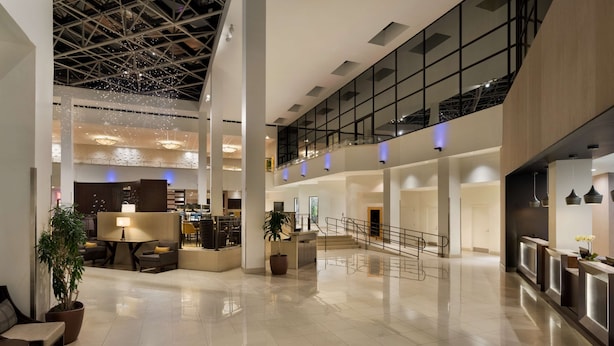 Eine geräumige Lobby mit hoher Decke, moderner Beleuchtung und einer Treppe zu einer oberen Ebene.