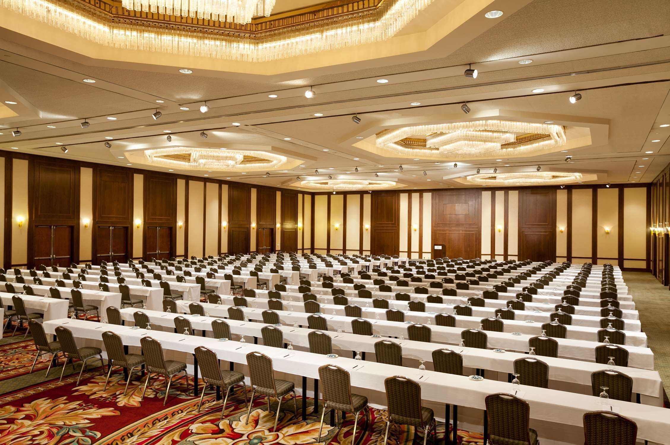 A large conference room with rows of tables and chairs, equipped with nameplates and water glasses.