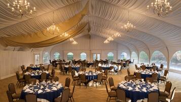 A large tented event space with round tables set for dining, chandeliers hanging from the ceiling, and large windows along the walls.