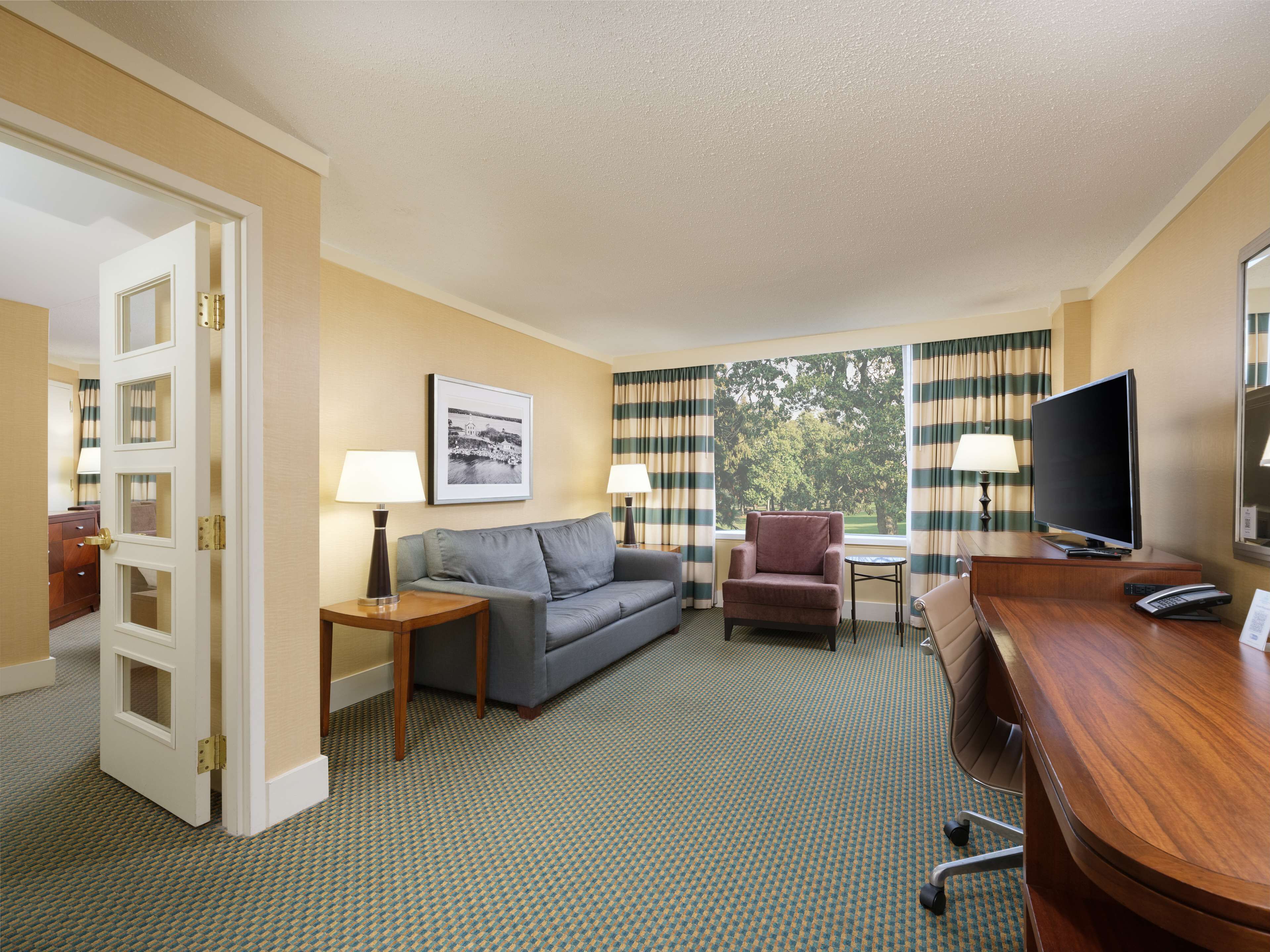 Habitación de hotel con sofá, sillón, televisión y escritorio con teléfono.