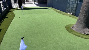 A golf course with artificial green turf, a flagstick, and a stone wall. - Surf City Inn and Suites (Santa Cruz)