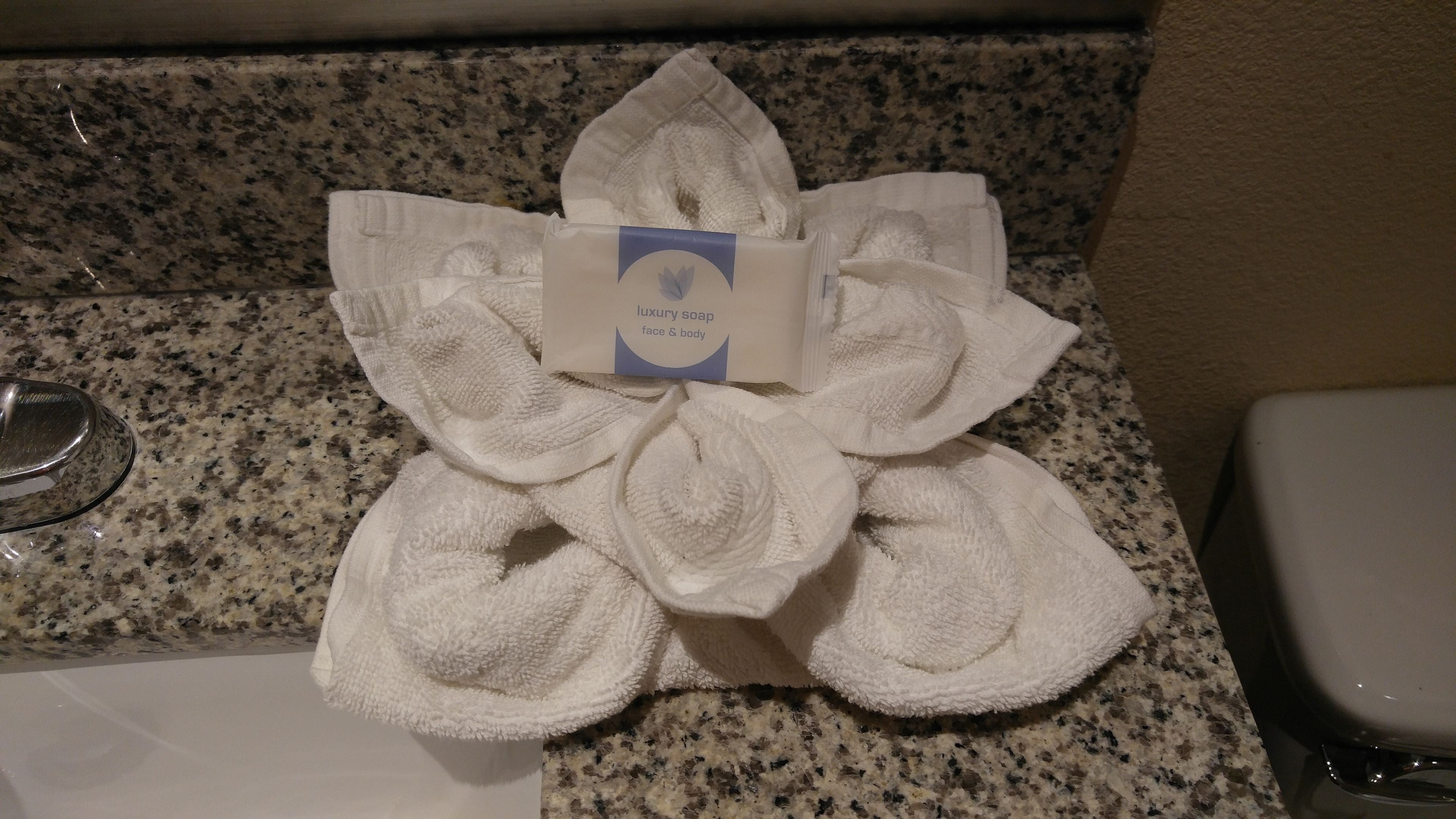 A towel arrangement in the shape of a flower on a granite countertop.