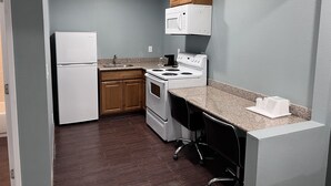 A compact kitchen with a refrigerator, stove, microwave, and wooden cabinets. - Surf City Inn and Suites (Santa Cruz)