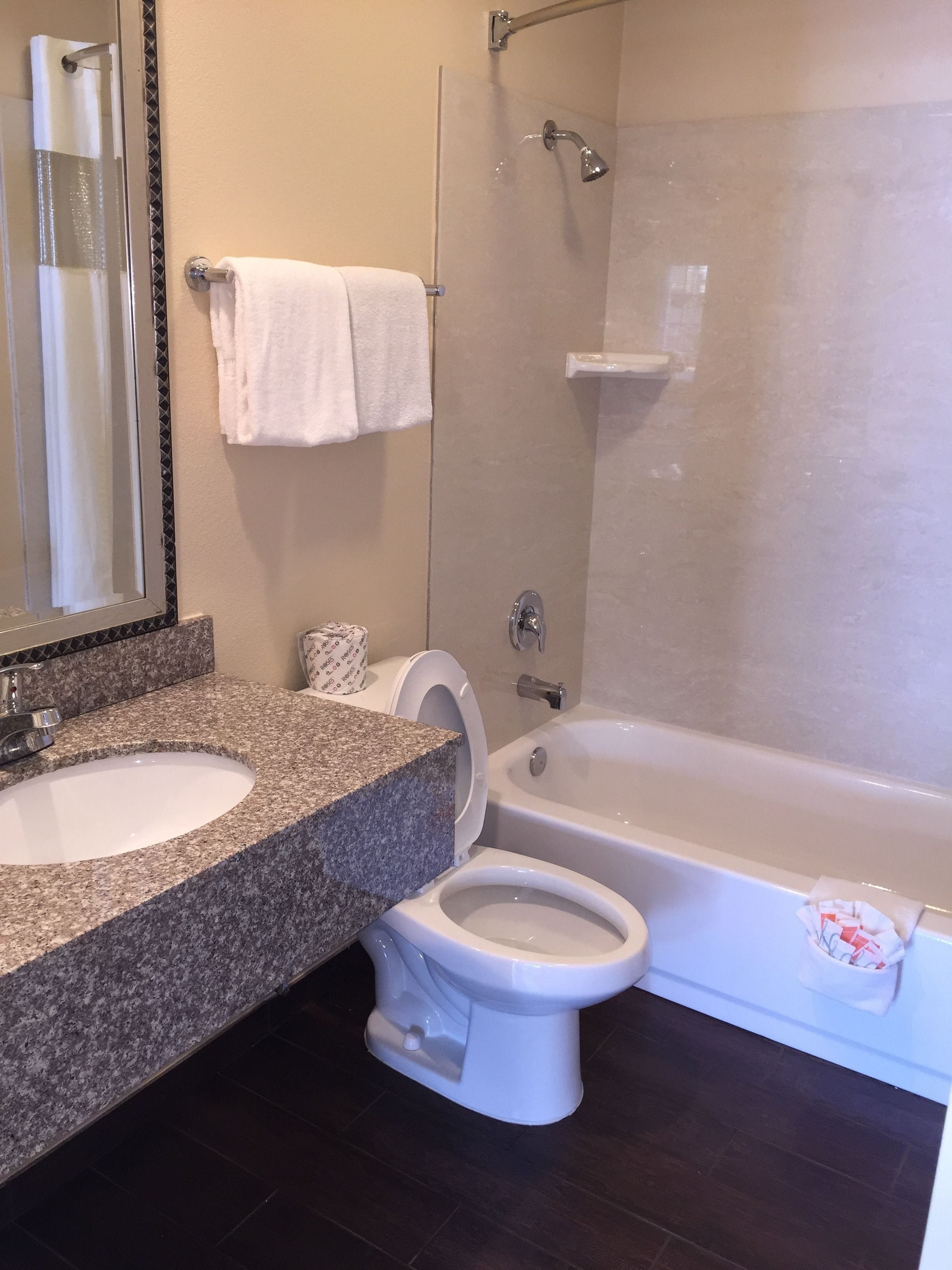 Un baño con lavamanos de encimera de granito, inodoro, bañera y cabina de ducha con mampara de vidrio.