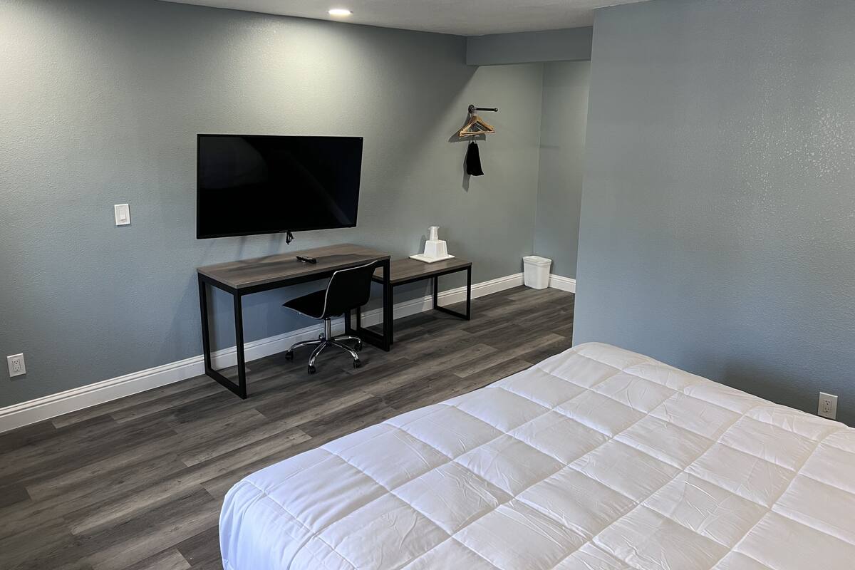 A bedroom with a bed, a desk with a chair, a television, and a small table.