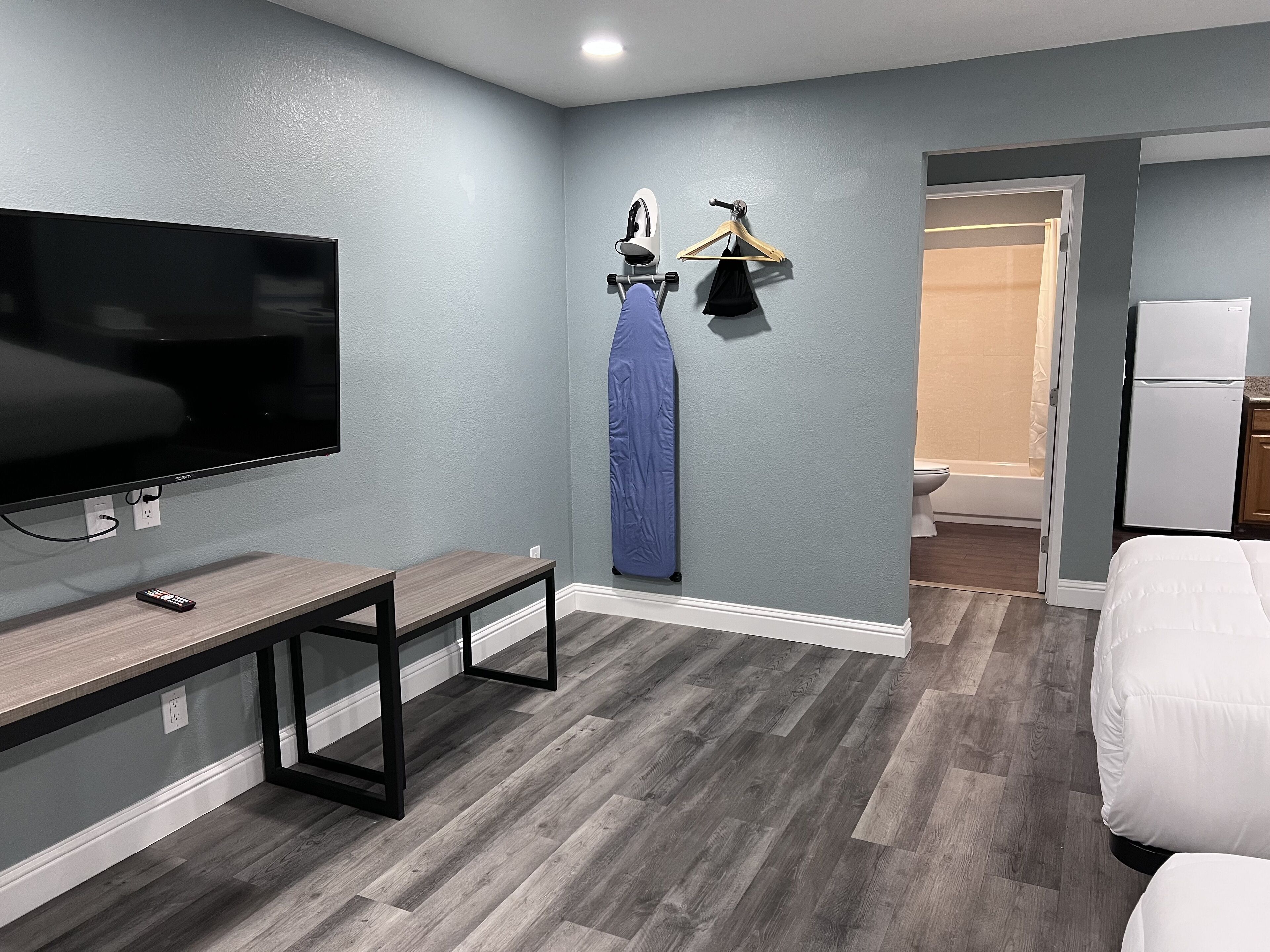 A modern hotel room with a flat-screen TV, a bench, a wardrobe, and a shower area.