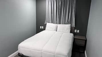 A neatly made bed with white bedding in a room with grey walls and a dark floor.