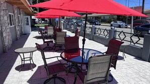 An outdoor patio with red umbrellas, wicker chairs, and a stone wall. - Surf City Inn and Suites (Santa Cruz)