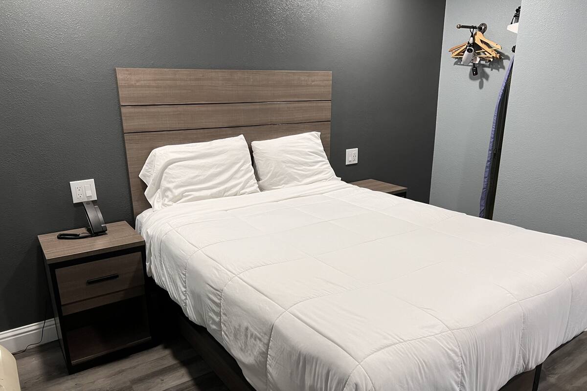 A neatly made bed with white bedding in a room with dark walls and wooden flooring.