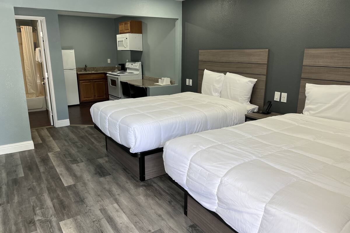A hotel room with two beds, a kitchenette, a shower, and a bathroom.