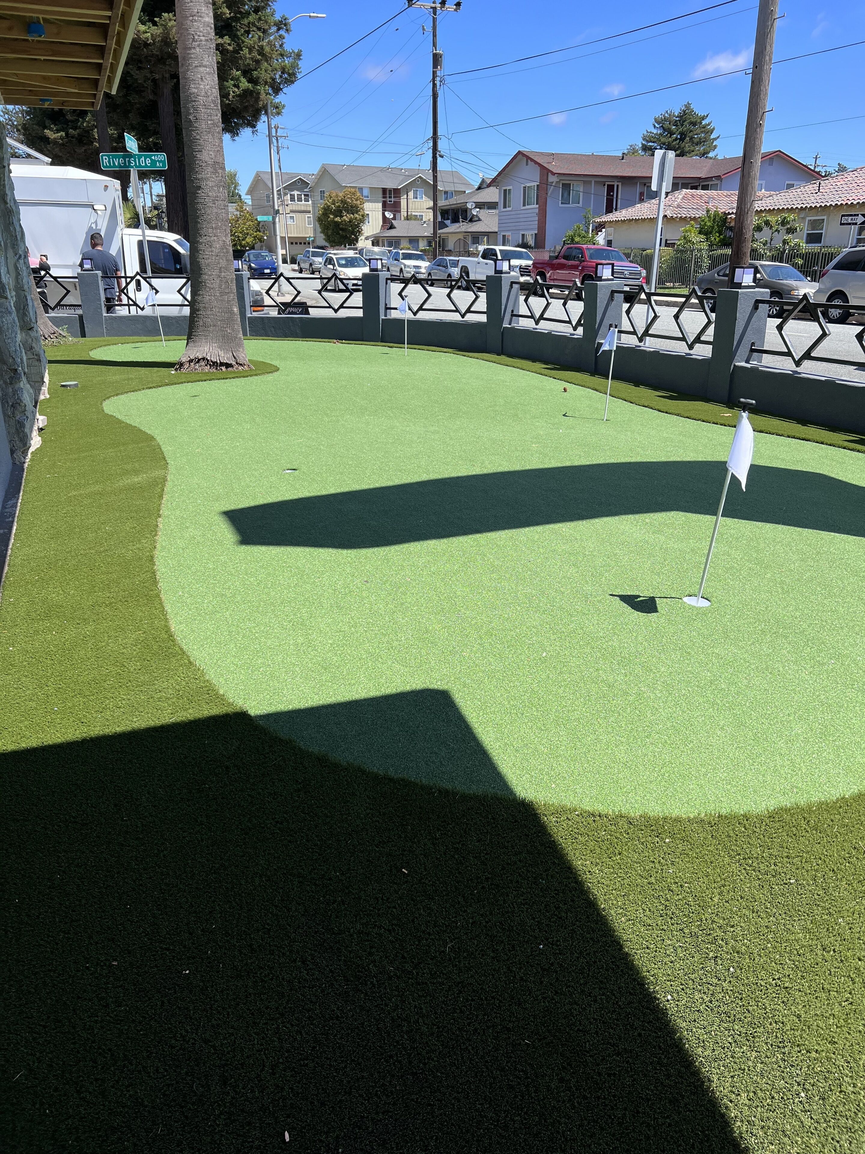 A golf course with artificial turf, a flagstick, and a wooden fence.
