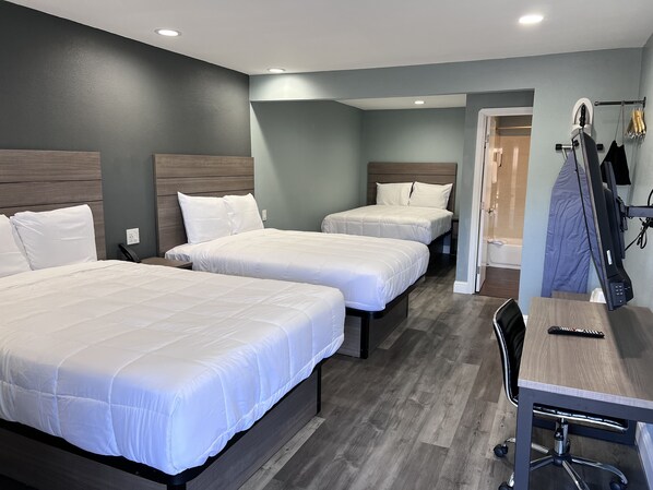 A hotel room with three beds, a desk, and a chair.