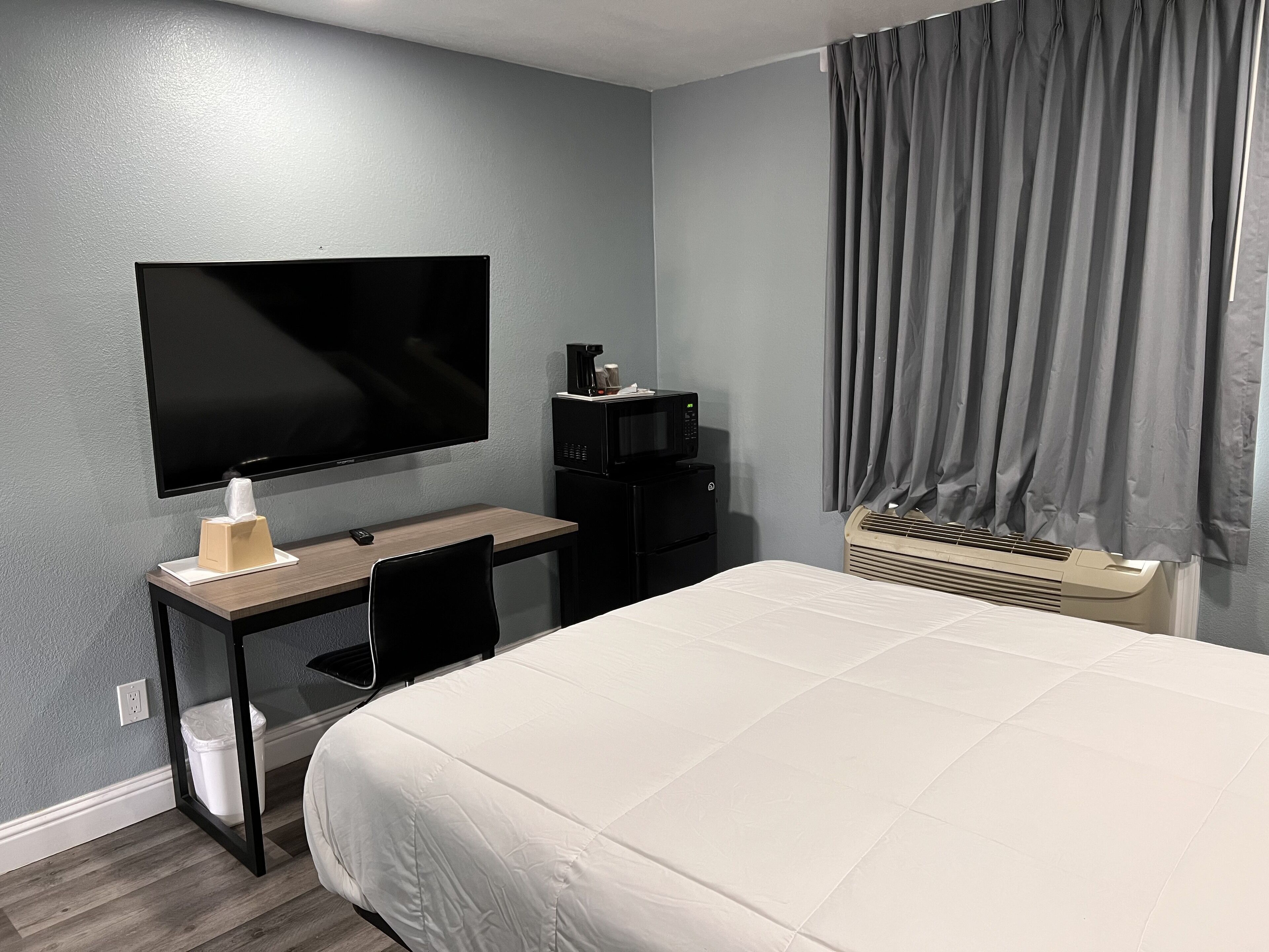 Ett hotellrum med en säng, ett skrivbord med en dator, en tv, en mikrovågsugn och en värmare.