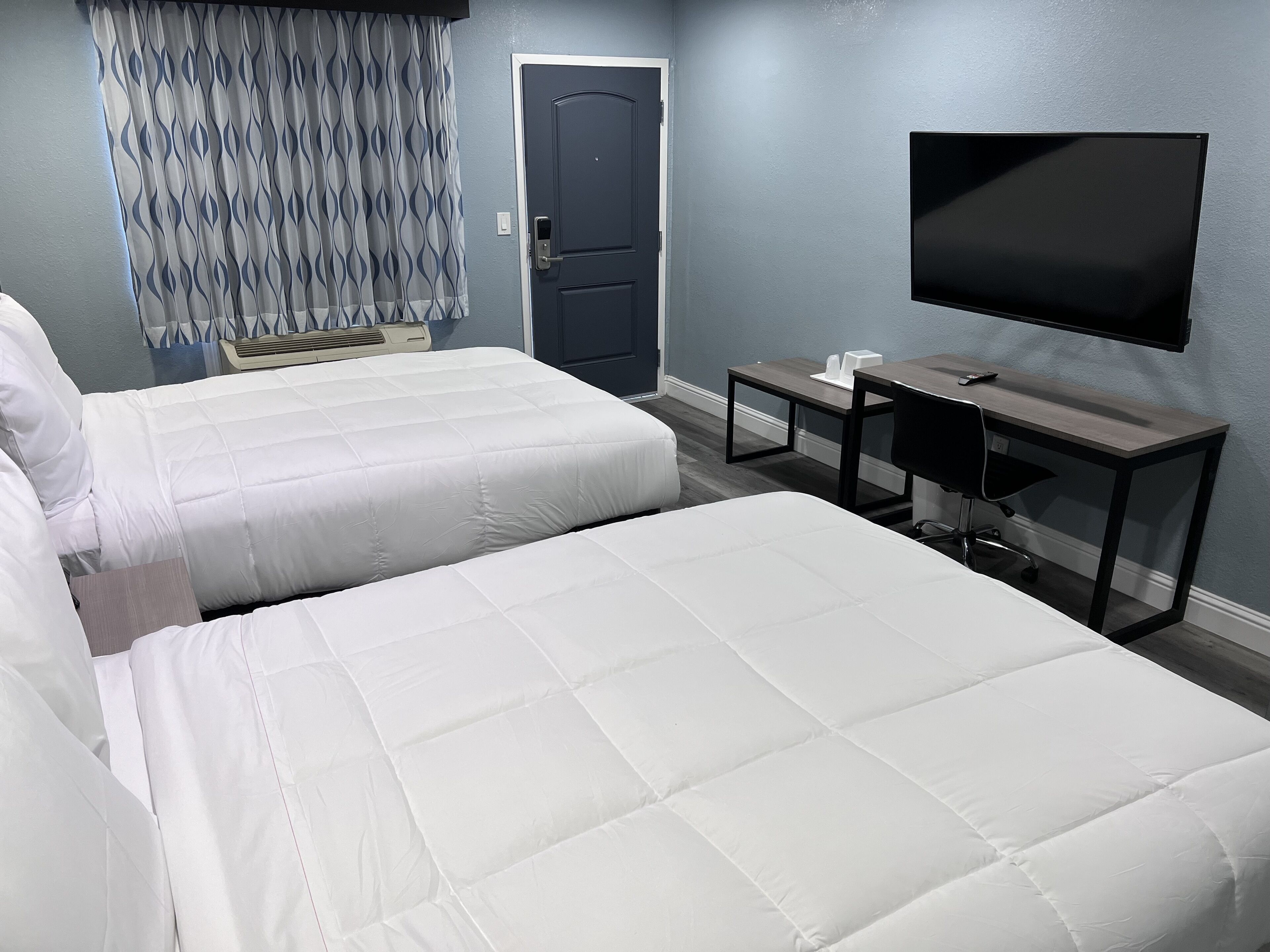 Une chambre d’hôtel avec deux lits, un bureau, une chaise, un téléviseur à écran plat et une porte.