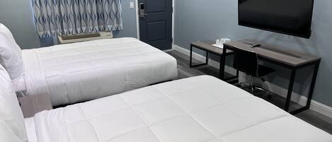 Une chambre d’hôtel avec deux lits, un bureau, une chaise, un téléviseur à écran plat et une porte.