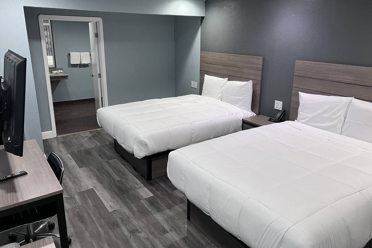 A hotel room with two beds, a desk, and a chair.