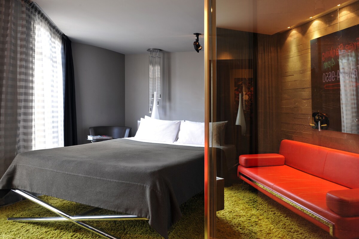 A modern hotel room with a large bed, a red sofa, and a large mirror on the wall.