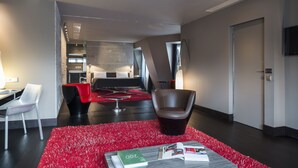 A modern hotel lobby with a red carpet, a dining area with a black table and chairs, a leather armchair, and a flat-screen TV mounted on the wall. - Hôtel Sezz Paris (Paris)