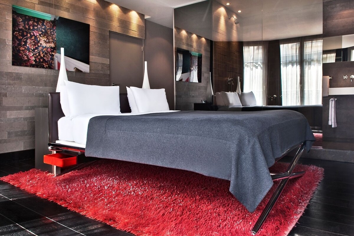 A modern bedroom with a large bed, a red shag rug, and a dark wood wall.