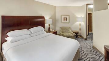 A hotel room with a large bed, two bedside tables, a chair, and a framed picture on the wall.