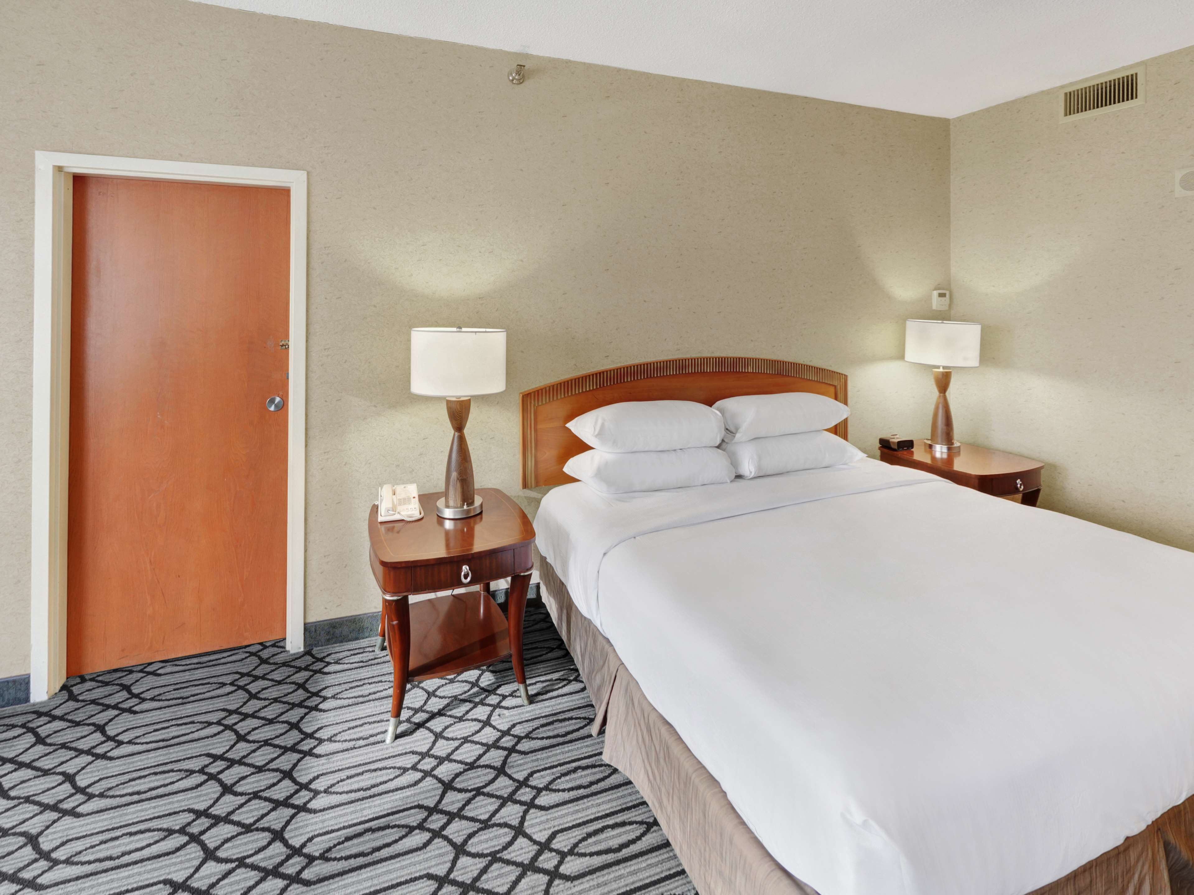 Habitación de hotel con cama de madera, dos mesitas de noche con lámparas, un teléfono y una alfombra estampada.