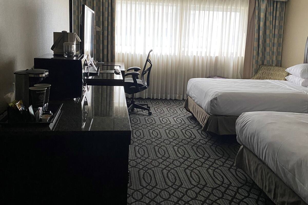 Ein Hotelzimmer mit Schreibtisch, zwei Betten, einem gemusterten Teppich und einem großen Fenster mit Vorhängen.