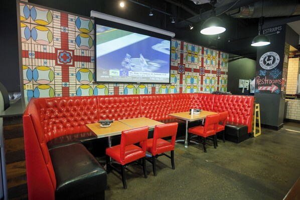 A sports bar with red leather booths, a large screen for viewing games, and a sign indicating the location of restrooms. - DoubleTree by Hilton Hotel St. Paul Downtown (St. Paul)