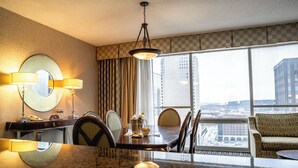 Hotelkamer met een eethoek, een groot raam met stadszicht, een ronde spiegel en een kroonluchter.