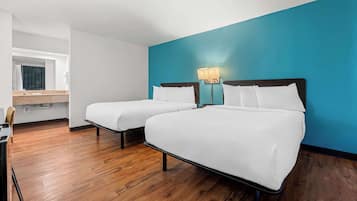 A hotel room with two single beds, a wooden floor, a blue accent wall, and a small desk with a chair.