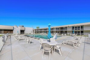 A pool area with lounge chairs and umbrellas, a clear blue sky, and a building with multiple balconies.