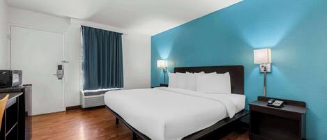 A hotel room with a bed, bedside tables, a desk, and a window with curtains.