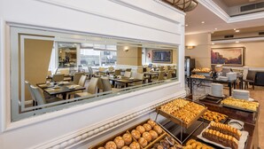 A spacious dining area with multiple tables and chairs, a buffet with various baked goods, and a large mirror reflecting the room. - Exe Hotel Colón (Buenos Aires)