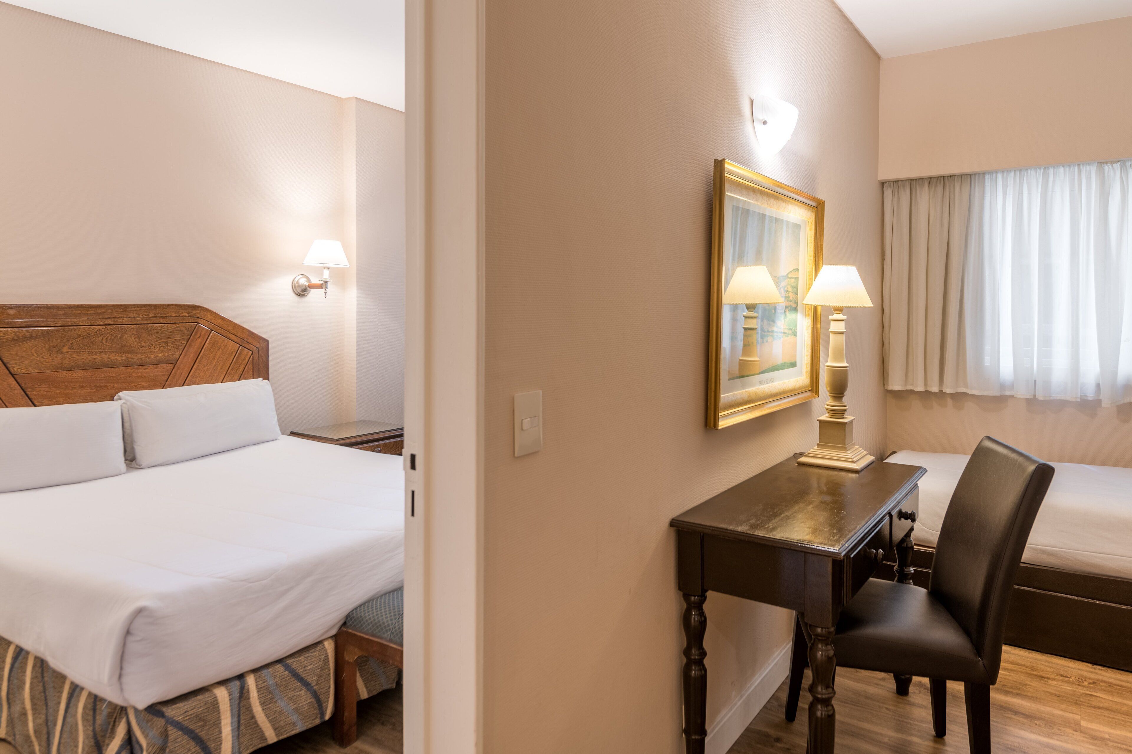 Una habitación de hotel con cama, escritorio, silla y ventana con cortinas.