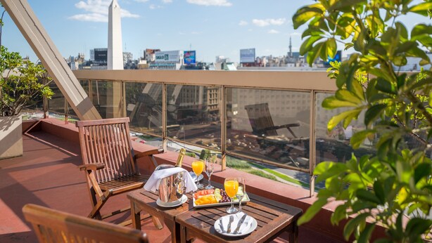 A balcony with a table set for breakfast, including a plate of fruit, a pitcher, and glasses of orange juice. - Exe Hotel Colón (Buenos Aires)