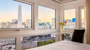 A hotel room with large windows offering a city view, a bed, a small table with a vase of flowers, and a chair. - Exe Hotel Colón (Buenos Aires)