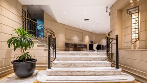 A marble staircase with black railings leading to a seating area with a potted plant. - Exe Hotel Colón (Buenos Aires)
