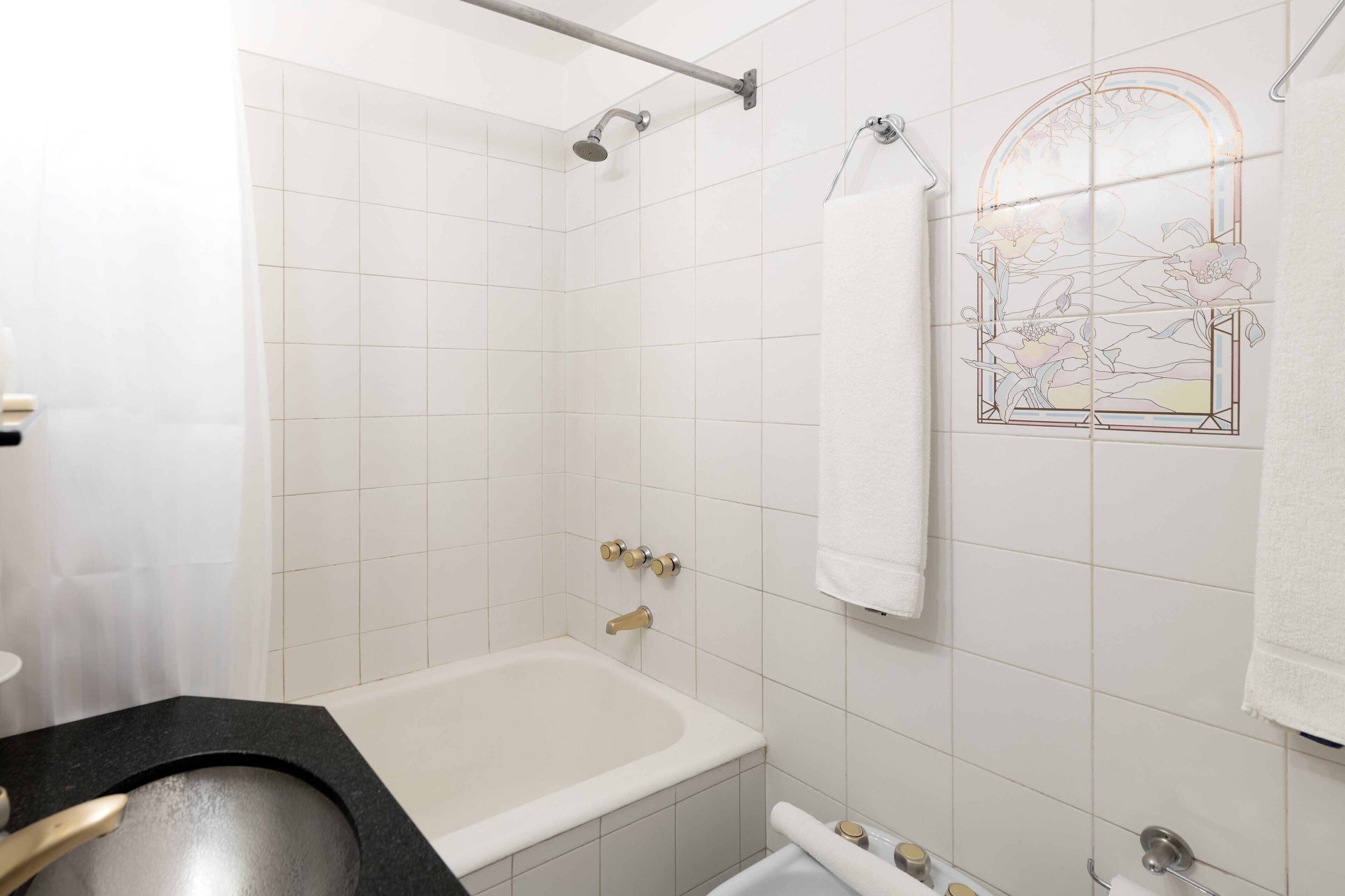 Un baño con bañera, ducha e inodoro. Se ve un perchero con una toalla blanca colgada.