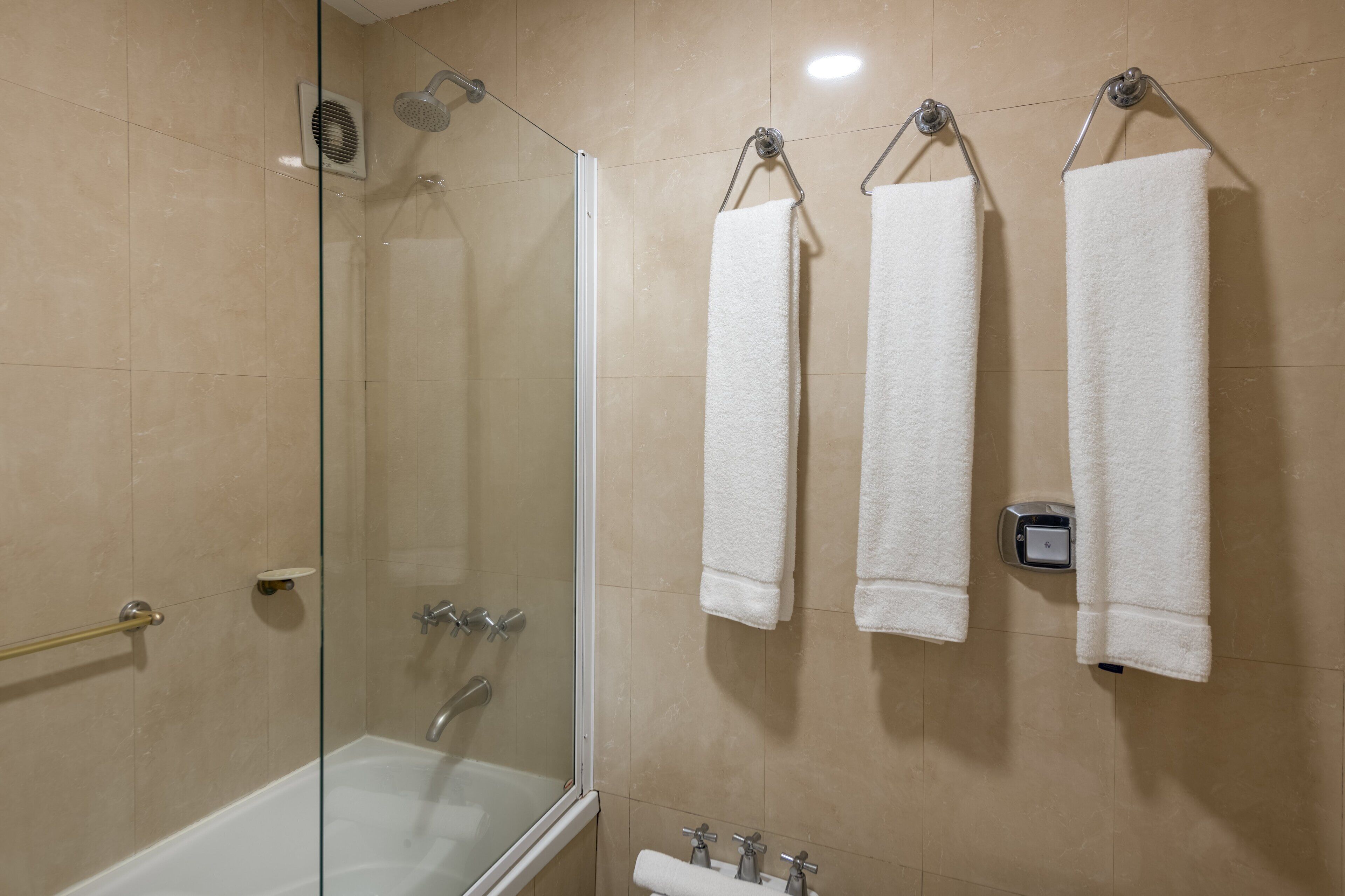 A bathroom with a glass-enclosed shower, a bathtub, and three white towels hanging on hooks.